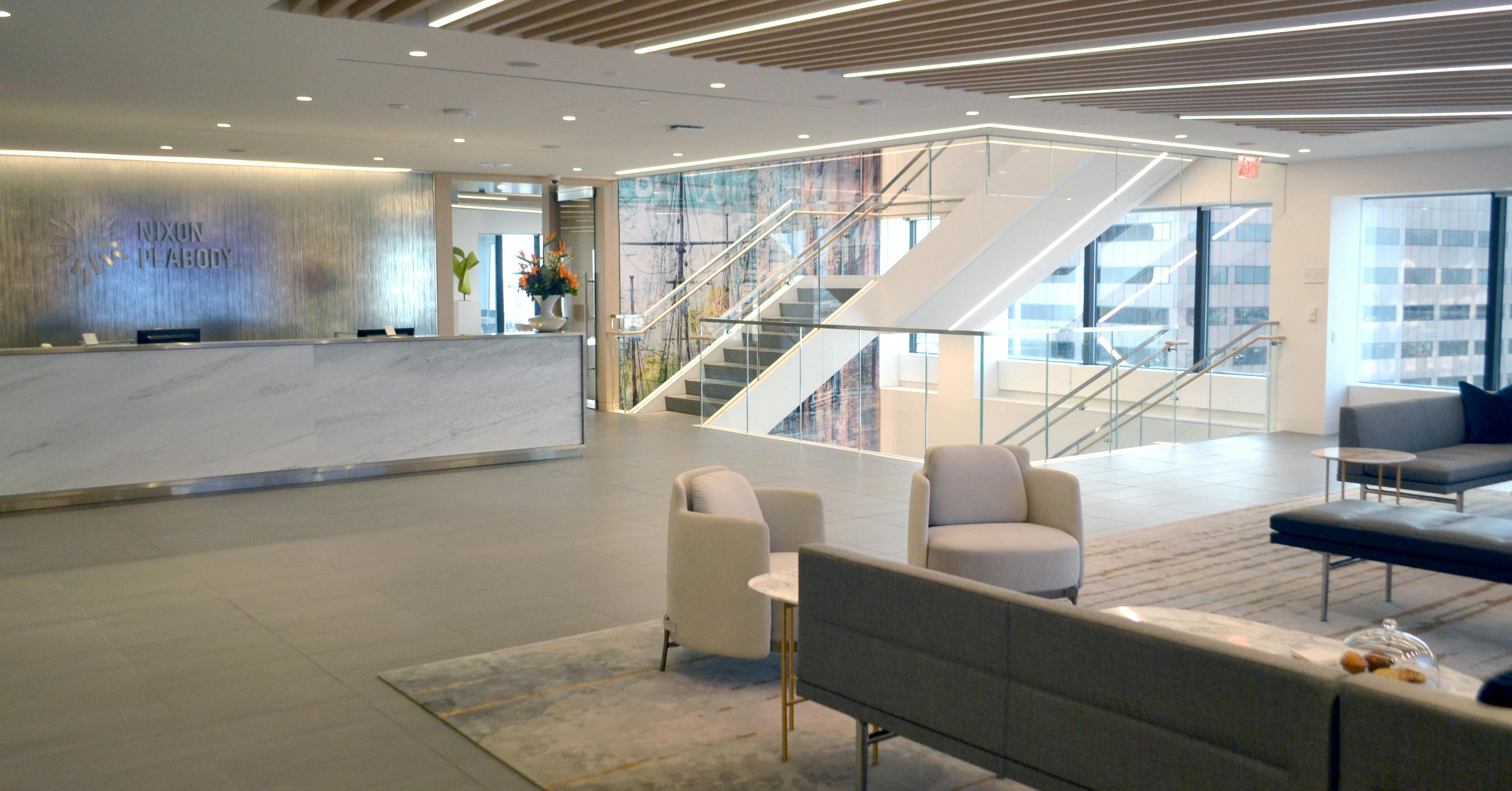 Interior of Nixon Peabody's Boston office lobby, showing a large reception desk in the background, a glass-enclosed stairwell to the right, and a lounge/waiting area in the foreground