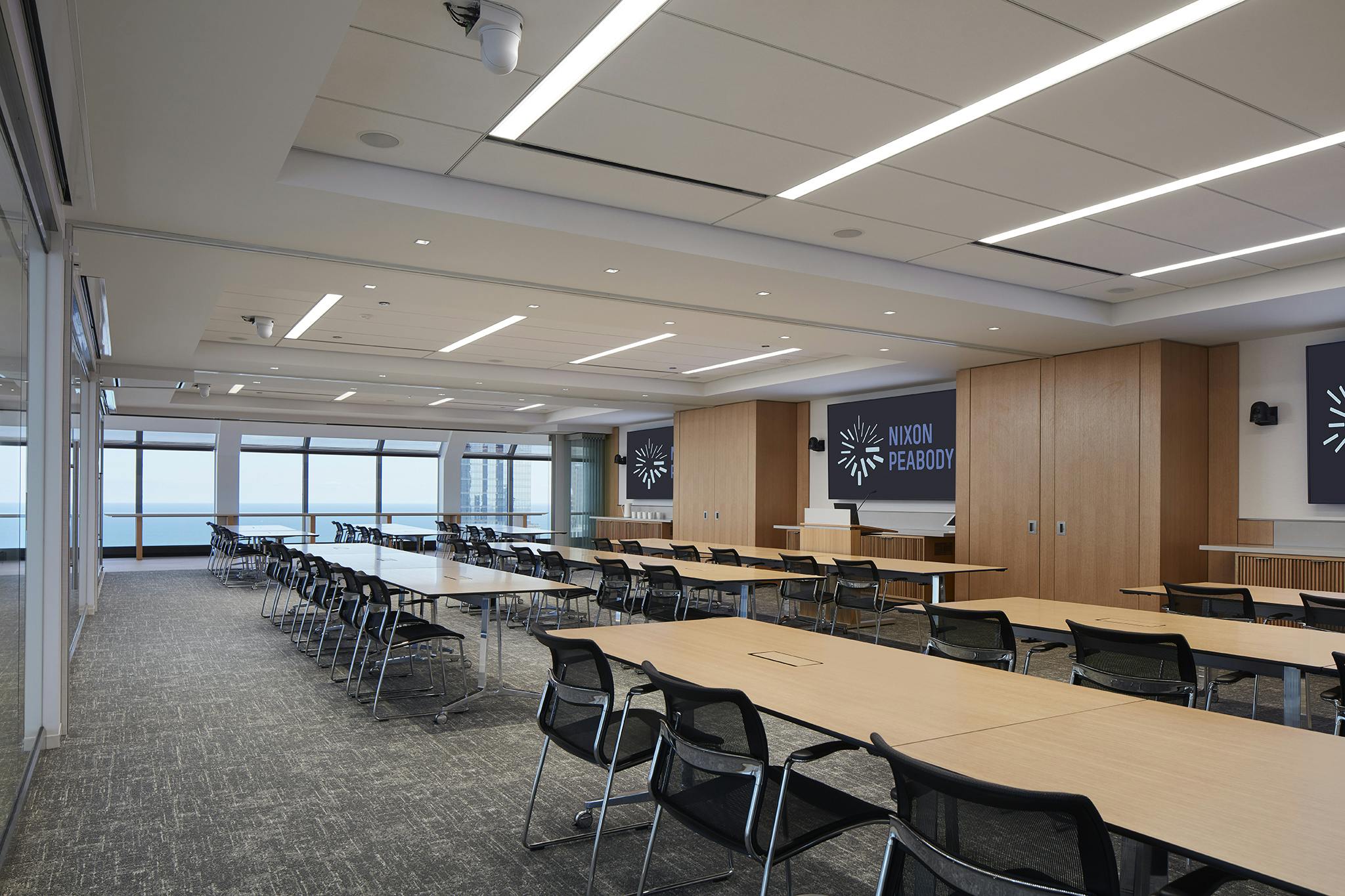 Conference room in Nixon Peabody's Chicago office, with several banks of conference tables, each with chairs, facing three large-screen TV monitors