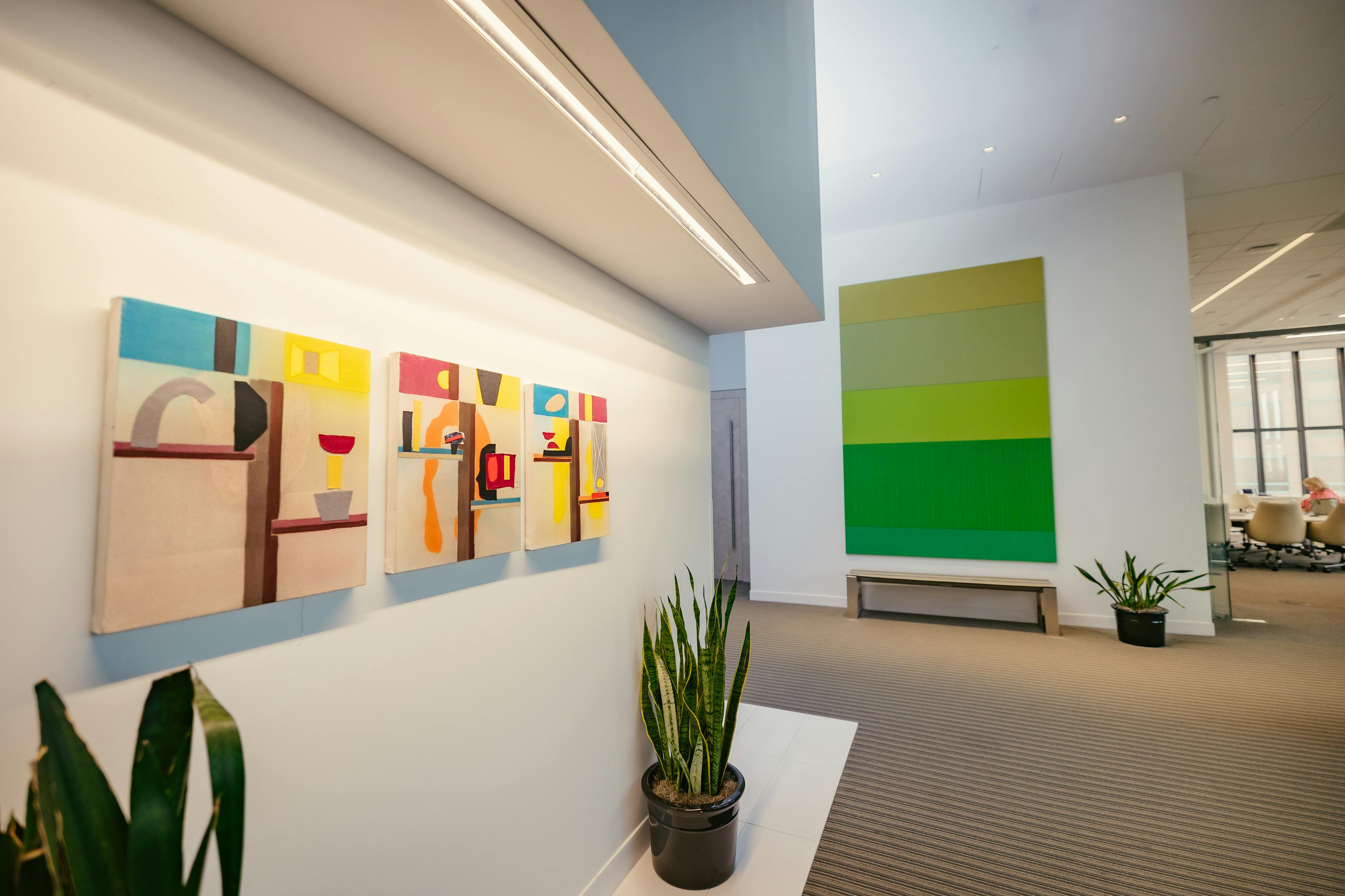 Hallway in Nixon Peabody's Los Angeles office, with three abstract paintings hanging in a row on the left wall, and another large-scale abstract painting hangs on another wall in the distance; potted plants decorate the floor