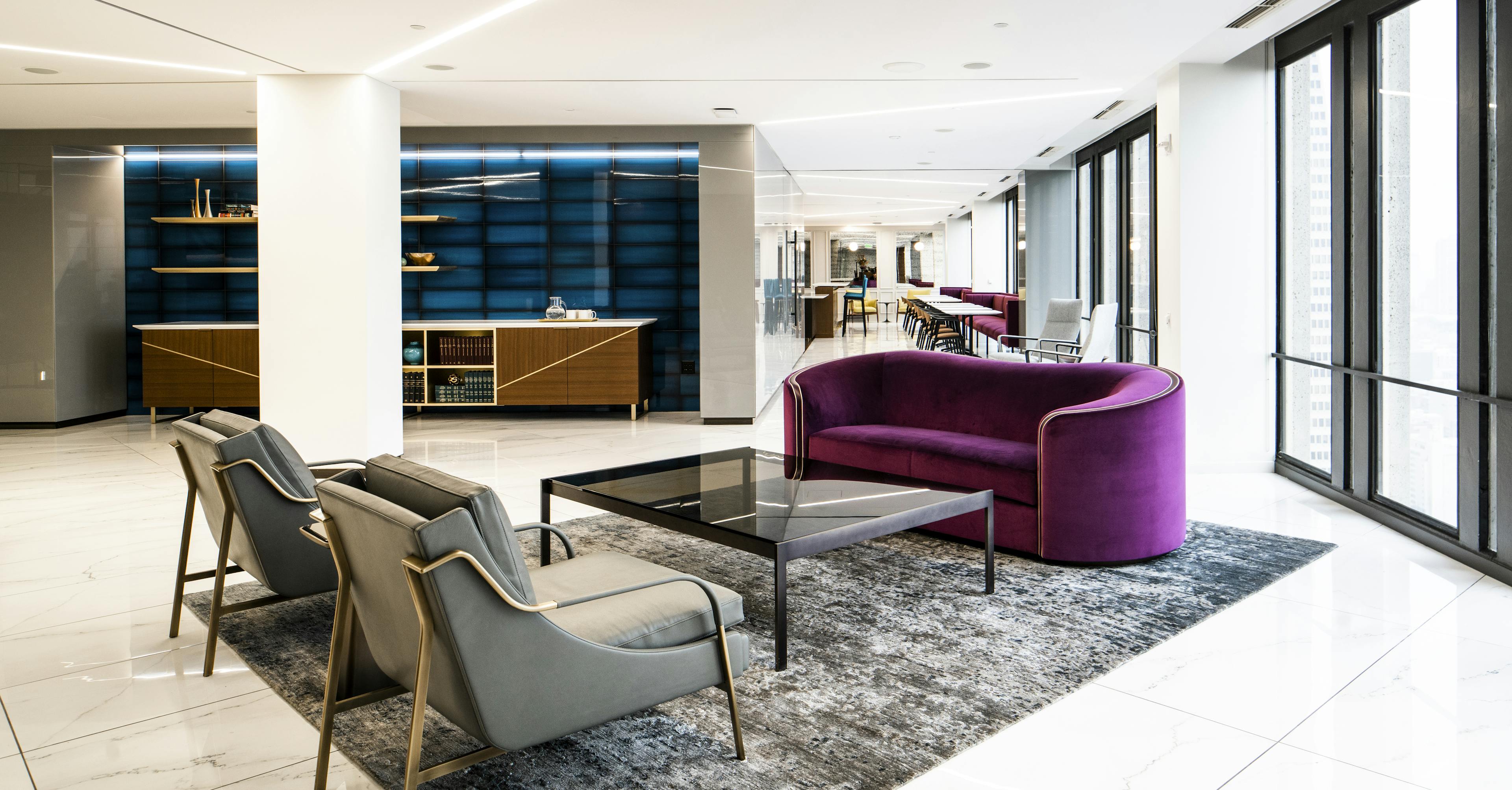 Interior shot of the seating area in Nixon Peabody's San Francisco office lobby, showing a purple couch, two grey chairs, and a glass coffee table, with a credenza in the background